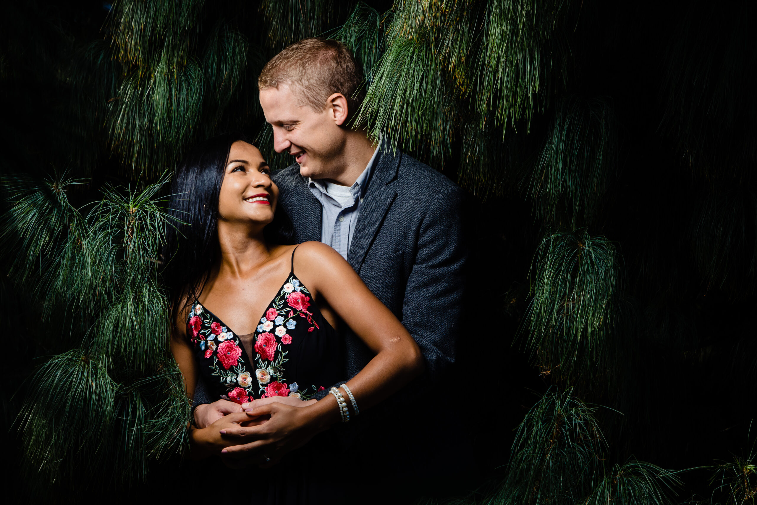 A romantic engagement moment captured in Washington DC as the couple gazes into each other's eyes with joyful smiles, surrounded by lush green trees. This enchanting scene was skillfully photographed by North Jersey wedding photographer Jarot Bocanegra