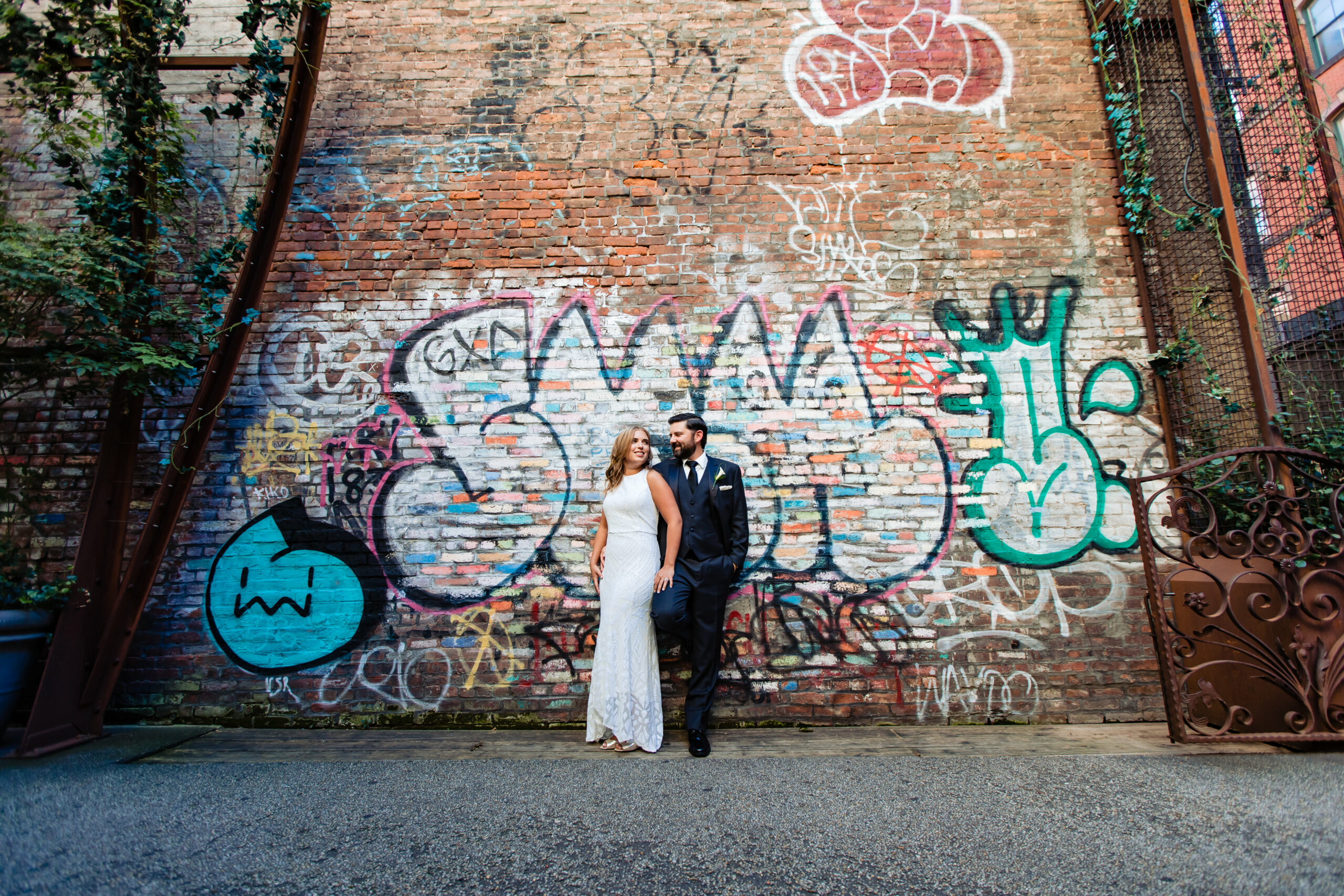 A stylish couple strikes a pose for a portrait against a vibrant graffiti wall art backdrop of The Nomo Soho hotel in New York City on their wedding day. The urban artistry adds a unique touch to their wedding portraits, skillfully captured by North Jersey wedding photographer Jarot Bocanegra