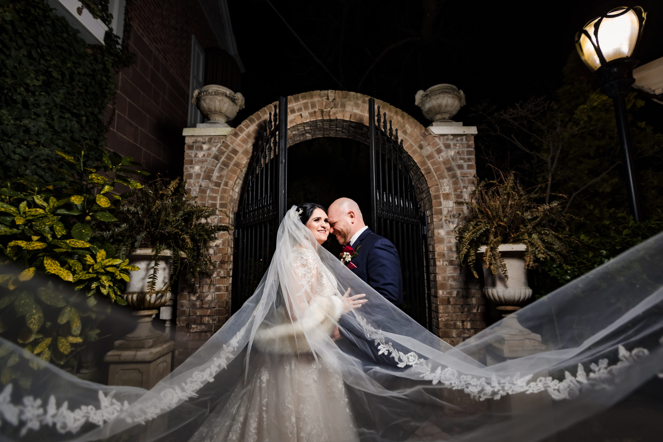 A captivating and creative night portrait of a joyful couple, both beaming with happiness, as the bride's veil gracefully floats in the air, creating a mesmerizing view. This enchanting moment was skillfully captured at The Brownstone by North Jersey wedding photographer Jarot Bocanegra
