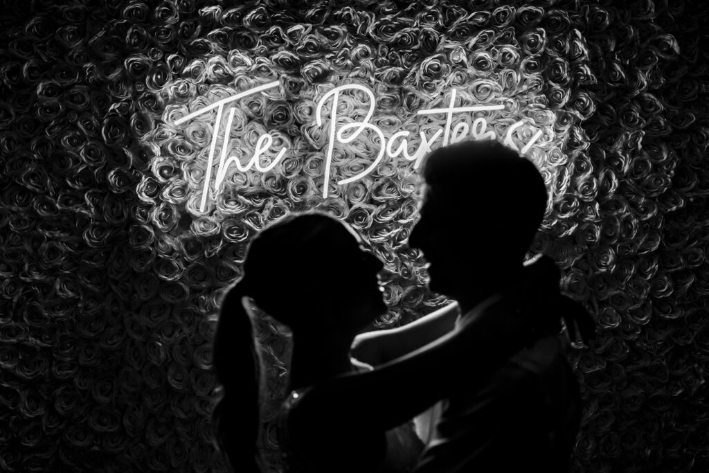 The bride and groom are captured by New Jersey Wedding Photographer Jarot Bocanegra, silhouetted against a wall with a neon sign.