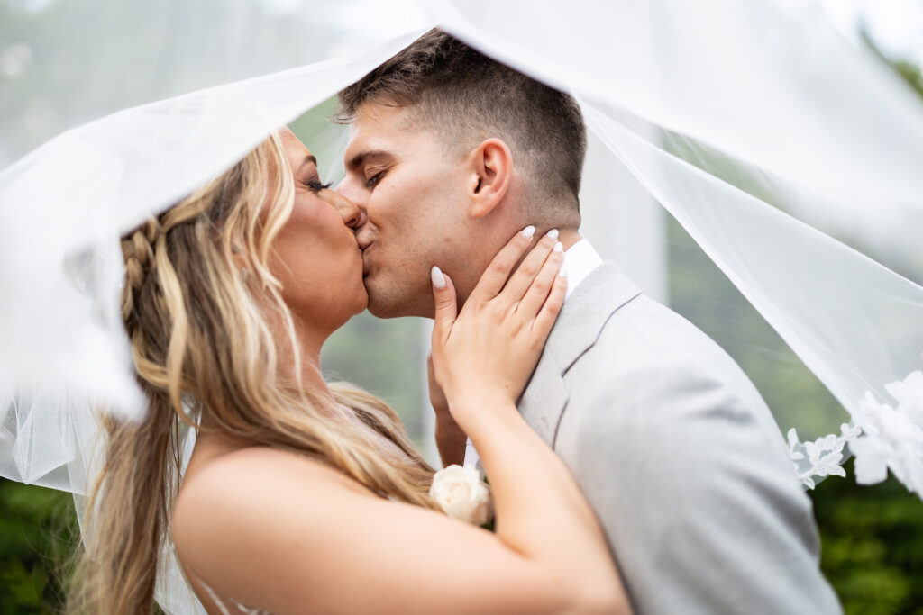 A bride and groom, captured by New Jersey Wedding Photographer Jarot Bocanegra, share a tender kiss under a veil.