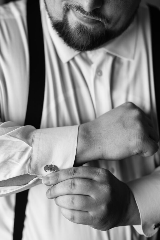 A black and white photo of a man adjusting his cufflinks, captured by New Jersey Wedding Photographer Jarot Bocanegra.