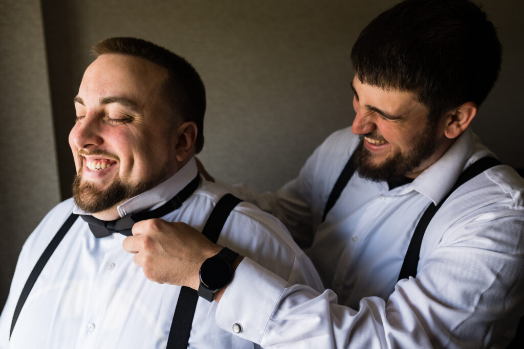 Two men captured by New Jersey Wedding Photographer Jarot Bocanegra, tying a bow tie in front of a mirror.