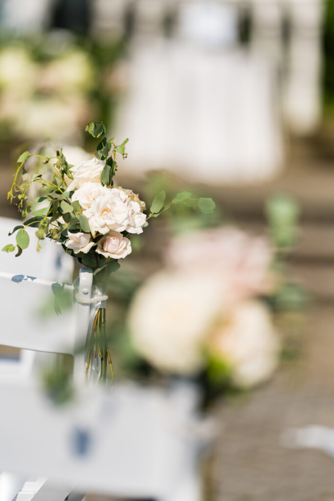 A row of white chairs with flowers on them captured by New Jersey Wedding Photographer Jarot Bocanegra.