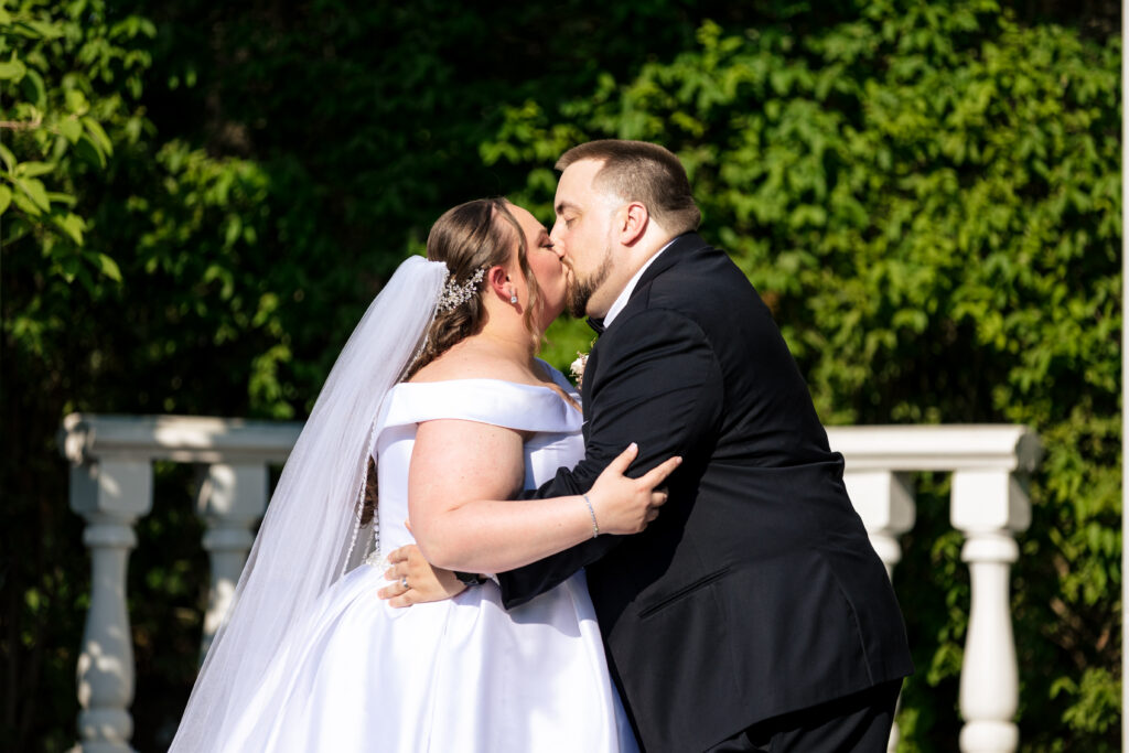 A bride and groom, captured by New Jersey Wedding Photographer Jarot Bocanegra, kissing in front of bushes.