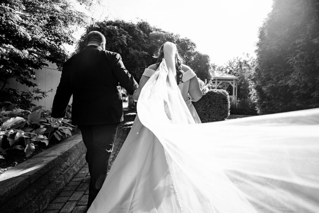 A bride and groom walking down a path with a veil, captured by New Jersey Wedding Photographer Jarot Bocanegra.