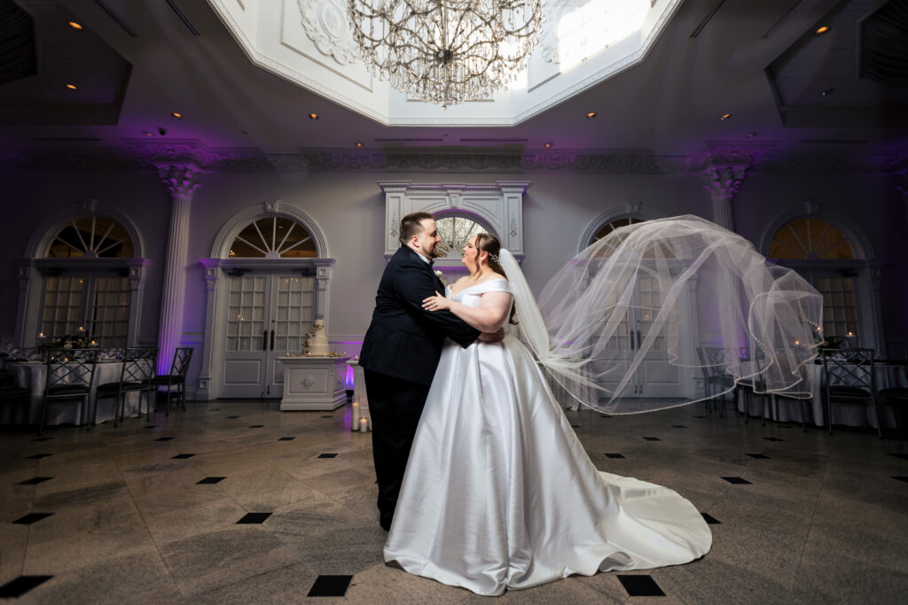 A bride and groom captured by New Jersey Wedding Photographer Jarot Bocanegra, standing in a room with a chandelier.