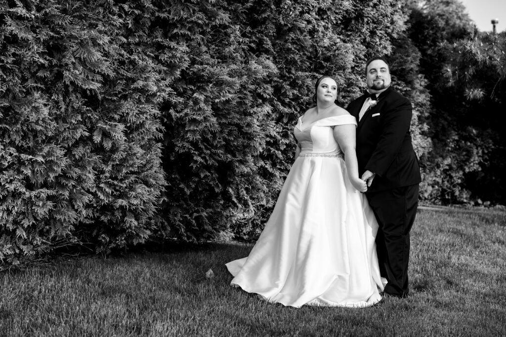 A bride and groom captured by New Jersey Wedding Photographer Jarot Bocanegra, posing in front of bushes.