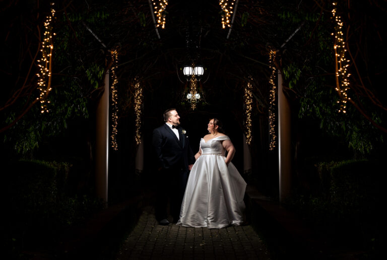 A bride and groom captured by New Jersey Wedding Photographer Jarot Bocanegra, standing under a string of lights.