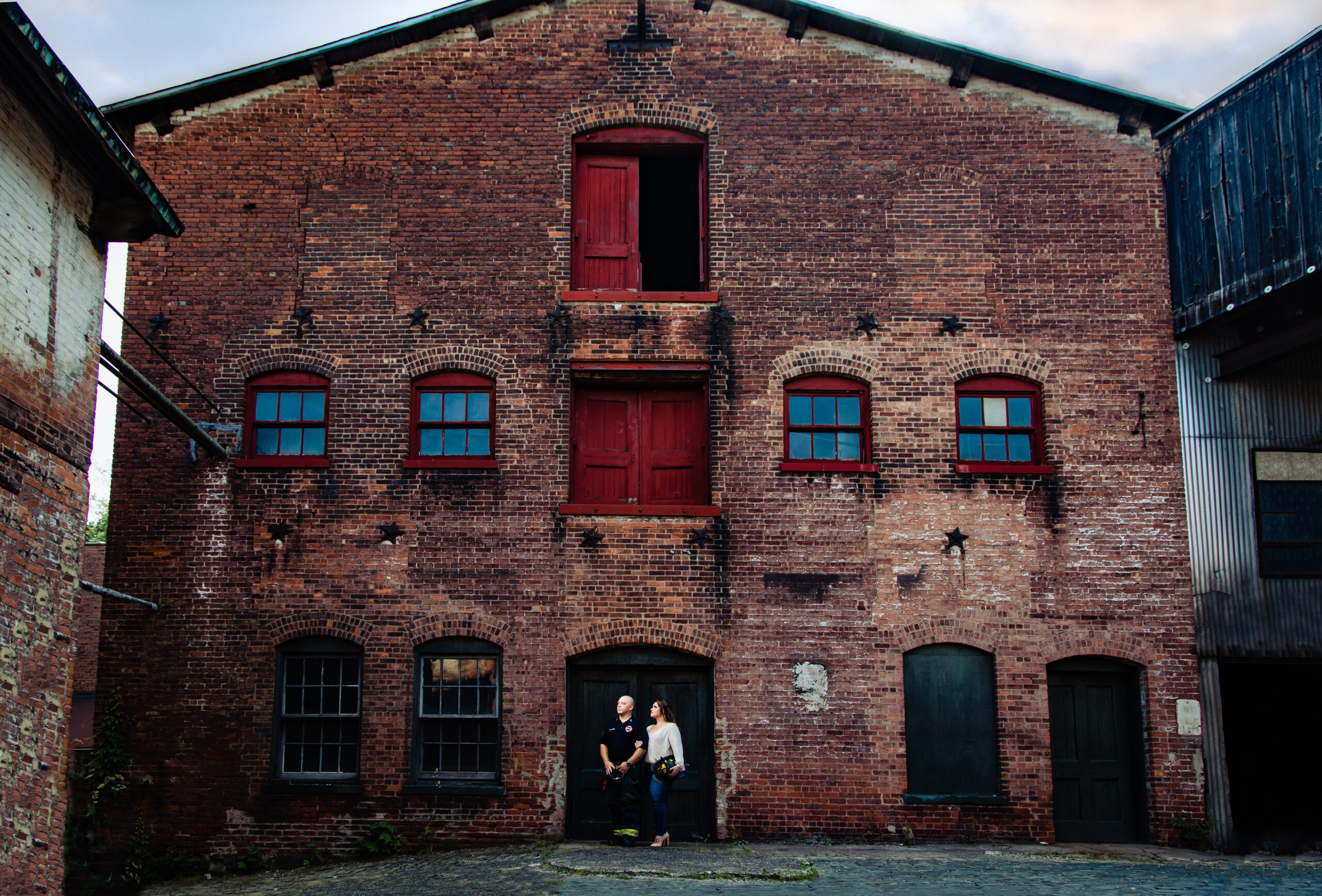 A creative engagement session portrait taken at the Art Factory in Paterson, NJ, with a stunning rustic building as the backdrop. This artfully composed scene was skillfully captured by Jarot Bocanegra Photography, showcasing the couple's love against a unique and picturesque setting