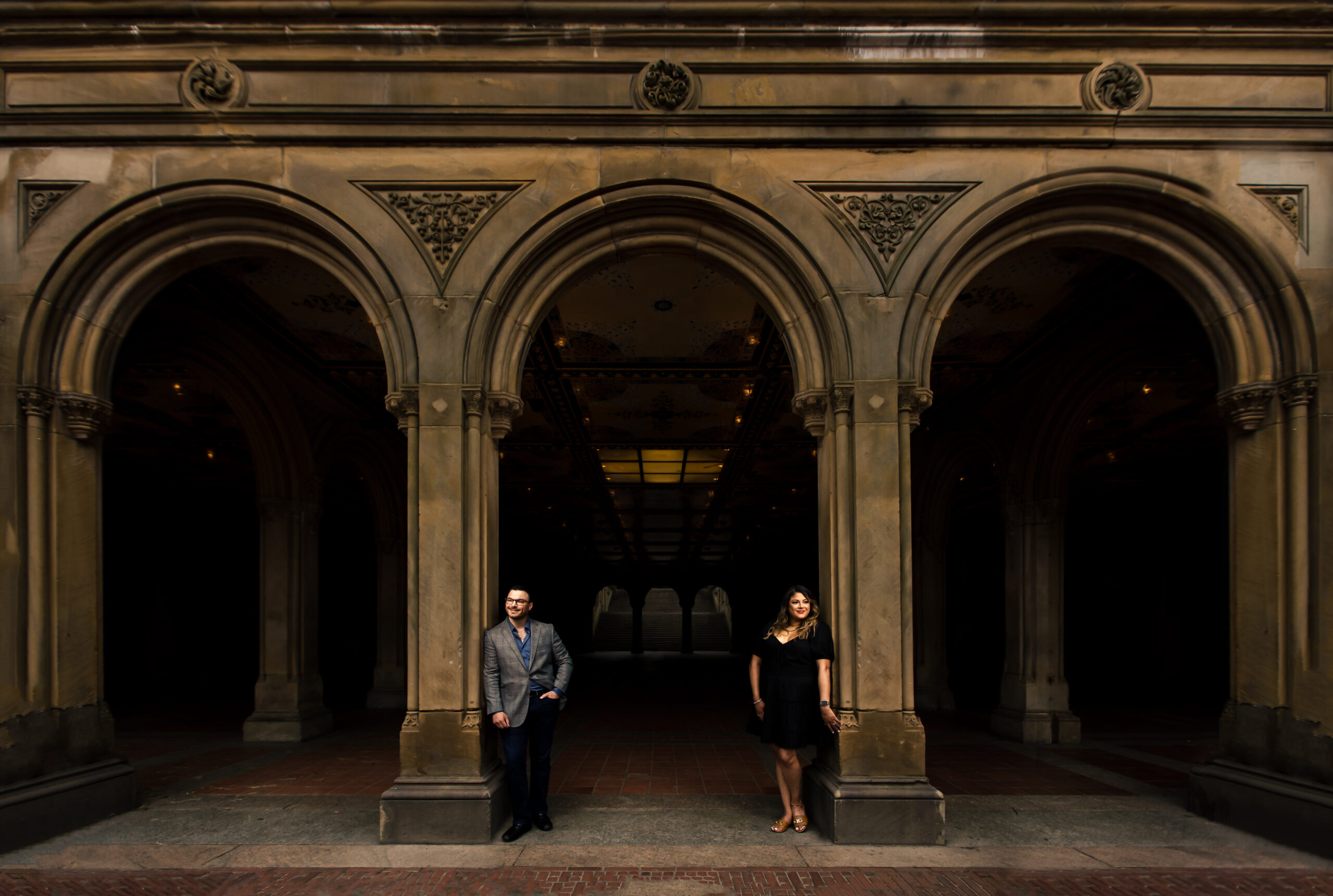 A creatively composed engagement session image of a couple at Bethesda Terrace in New York City, where the breathtaking architecture provides a stunning backdrop. This captivating scene was expertly photographed by North Jersey wedding photographer Jarot Bocanegra