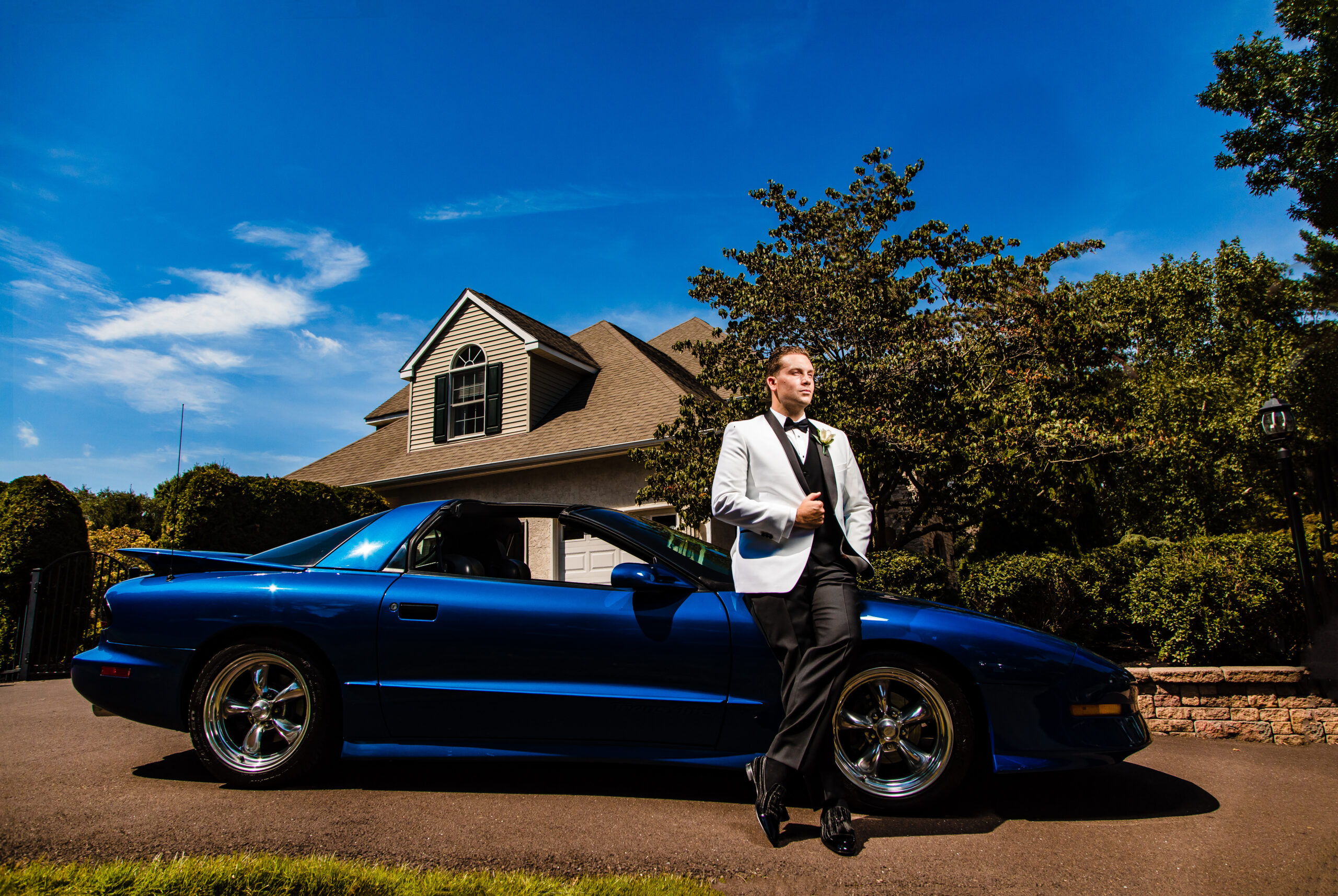 A man in a tuxedo captured by New Jersey Wedding Photographer Jarot Bocanegra next to a blue sports car.