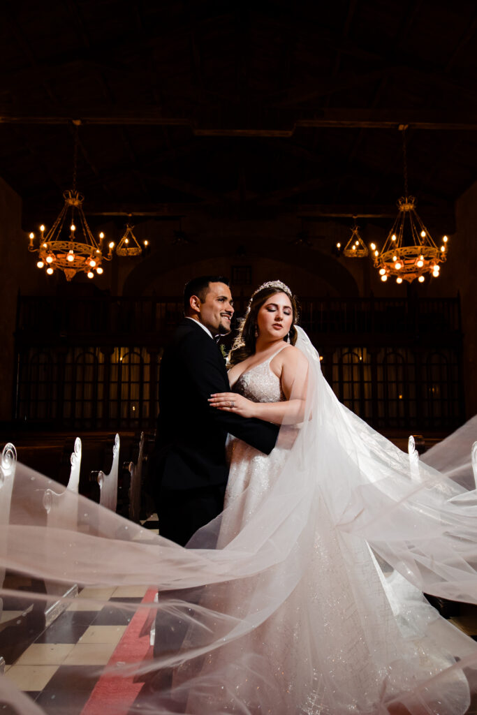 Captured by New Jersey Wedding Photographer Jarot Bocanegra, a bride and groom posing elegantly in front of a chandelier.
