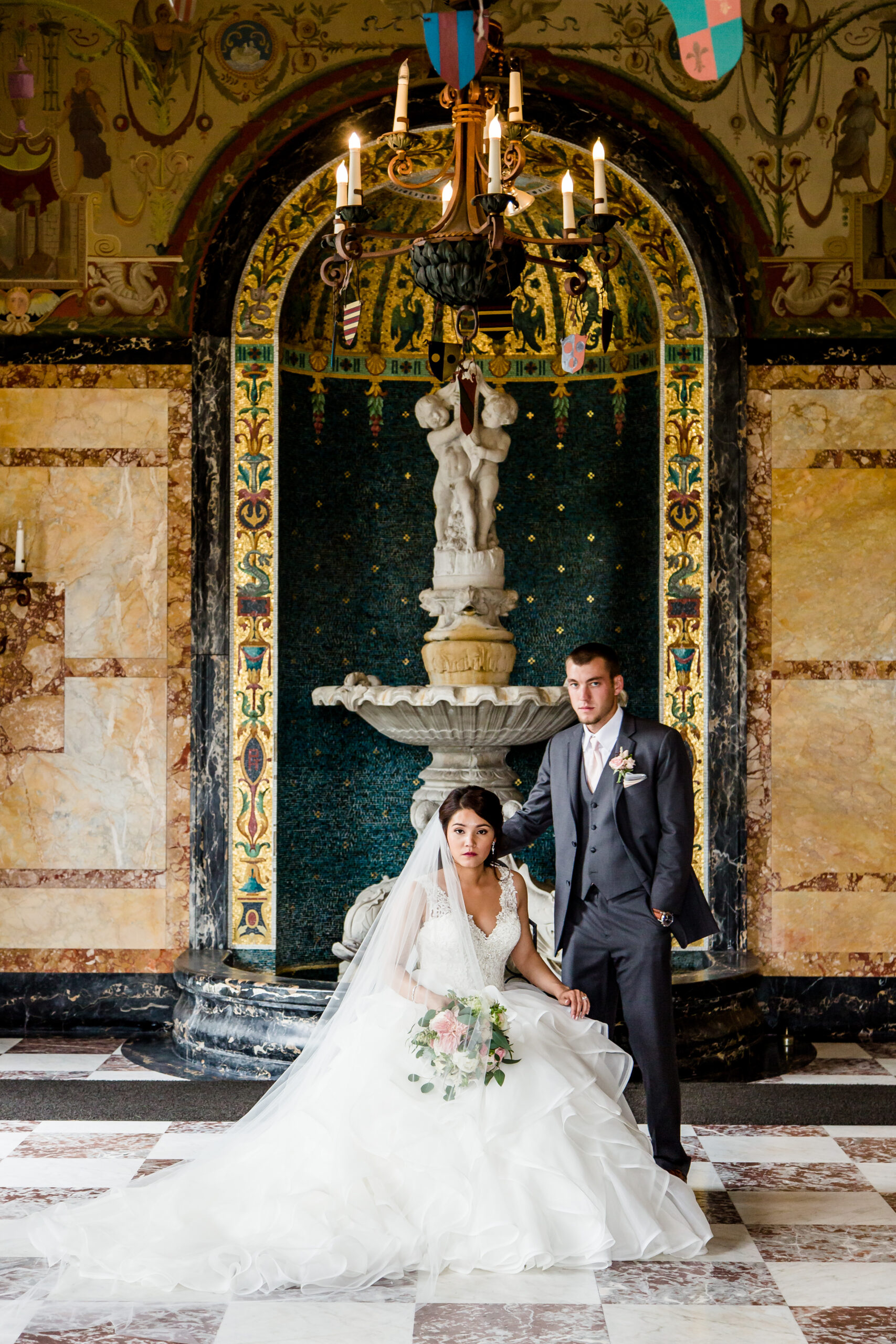 An elegant portrait of the bride seated with the groom standing right behind her in a glamorous room with a Spanish-inspired ambiance. The couple exudes sophistication and grace, capturing the essence of their special day, skillfully photographed by North Jersey wedding photographer Jarot Bocanegra