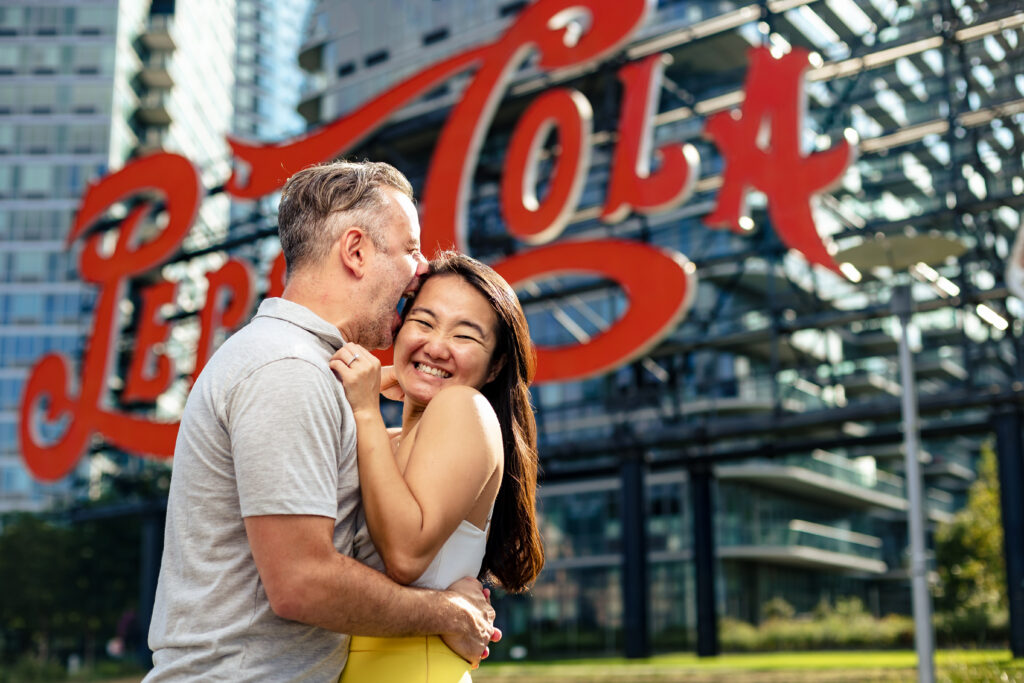 A couple embracing in front of a Coca-Cola sign, captured by New Jersey Wedding Photographer Jarot Bocanegra.