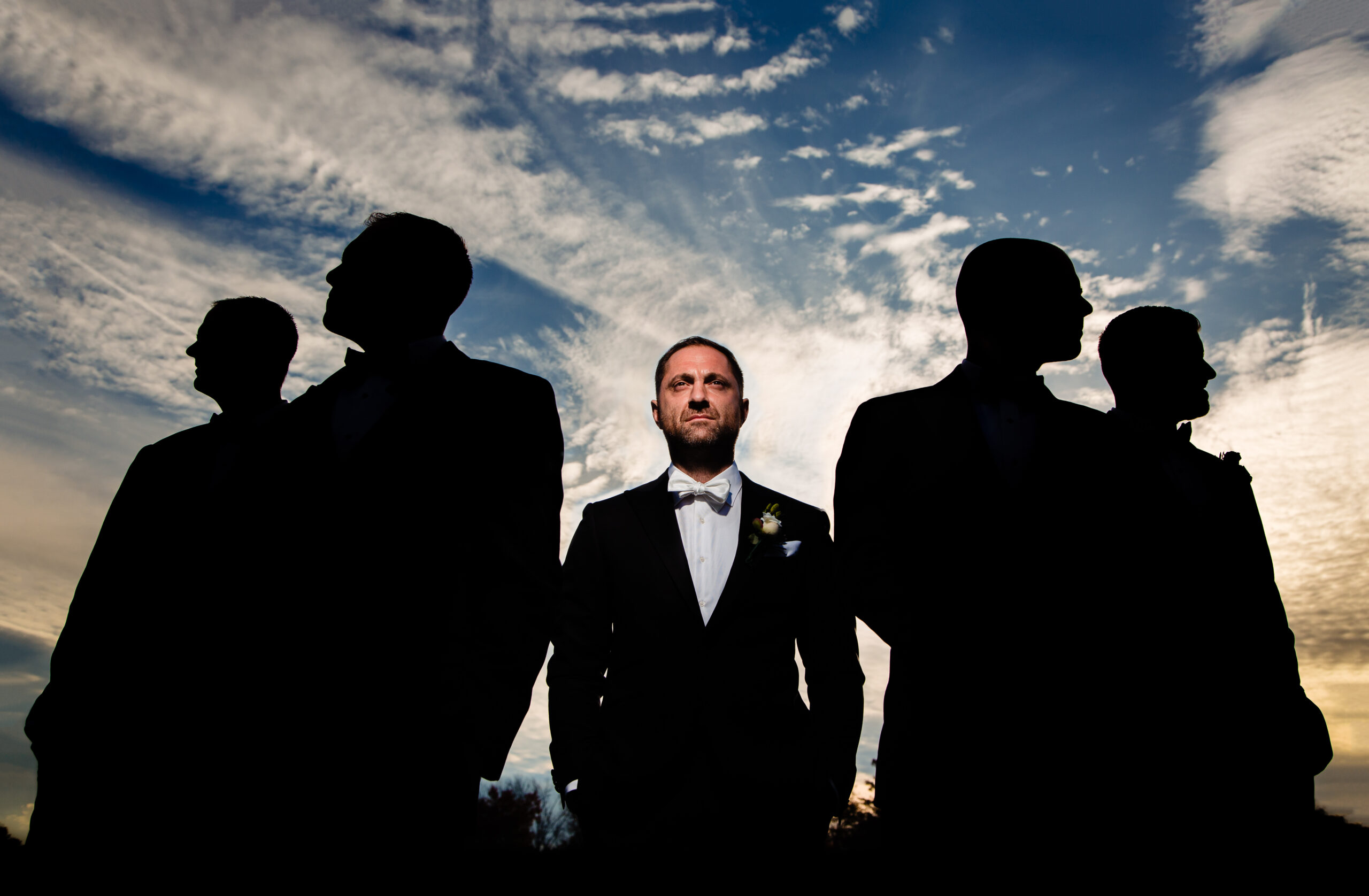 A creative portrait featuring the groom well-lit in the foreground, while his groomsmen are depicted in silhouette in the background. This artistic composition, skillfully captured by Jarot Bocanegra Photography, adds a unique touch to the wedding photography