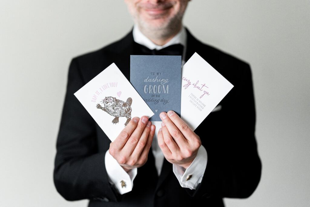 A man in a tuxedo holding three cards, captured by New Jersey Wedding Photographer Jarot Bocanegra.