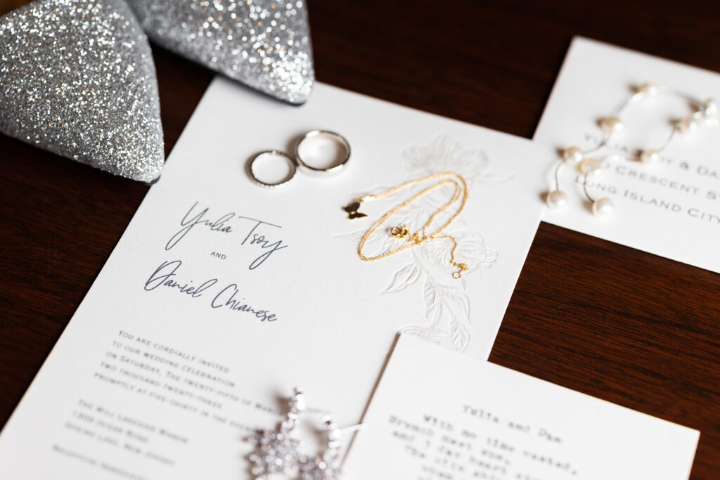 Wedding invitations and rings beautifully captured by New Jersey Wedding Photographer Jarot Bocanegra on a table.
