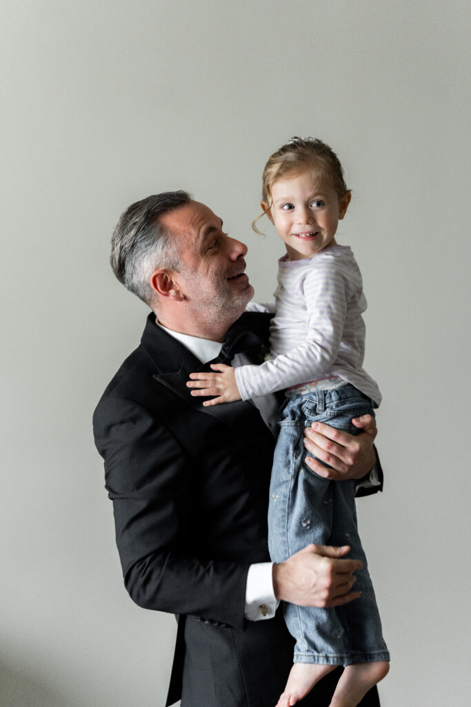 A man in a tuxedo captured by New Jersey Wedding Photographer Jarot Bocanegra, holding a little girl.