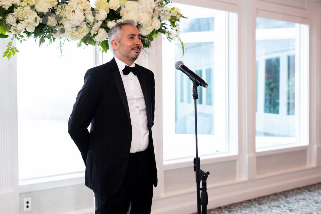 A man in a tuxedo captured by New Jersey Wedding Photographer Jarot Bocanegra, speaking into a microphone.