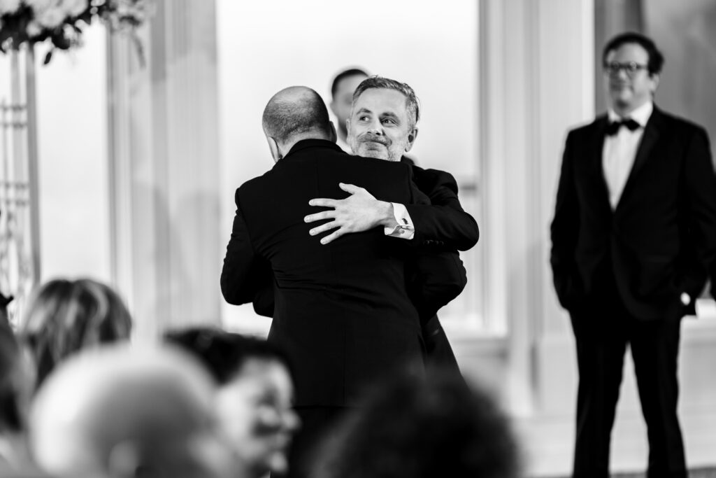 A man is hugging another man during a wedding ceremony, captured by New Jersey Wedding Photographer