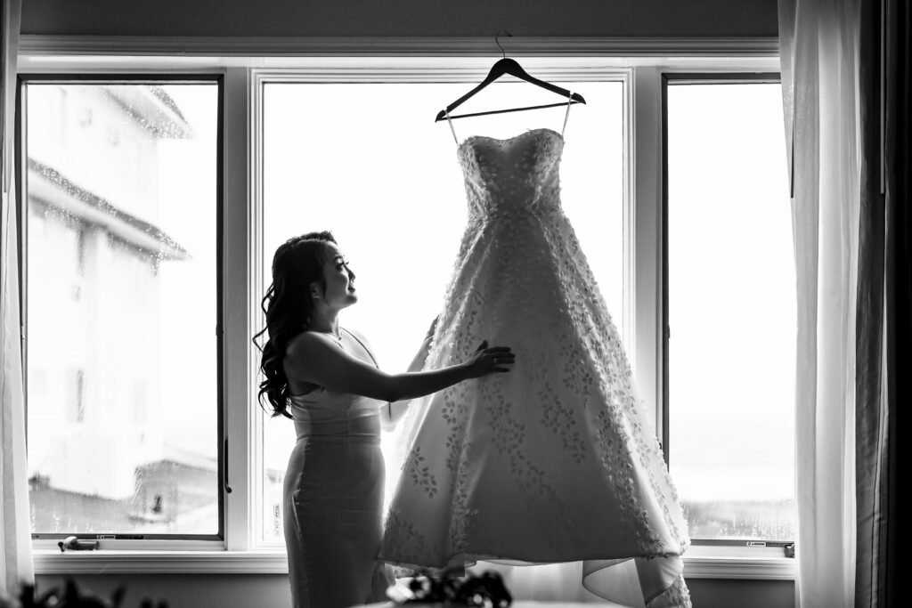 A bride putting on her wedding dress in front of a window, captured by New Jersey Wedding Photographer Jarot Bocanegra.