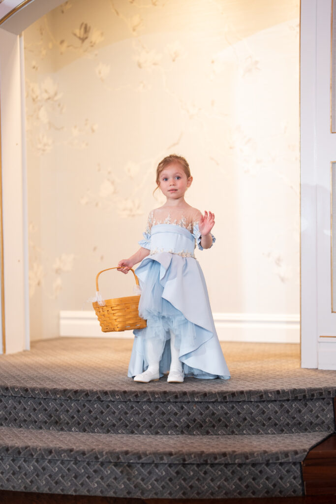 A little girl in a blue dress holding a basket captured by New Jersey Wedding Photographer Jarot Bocanegra.