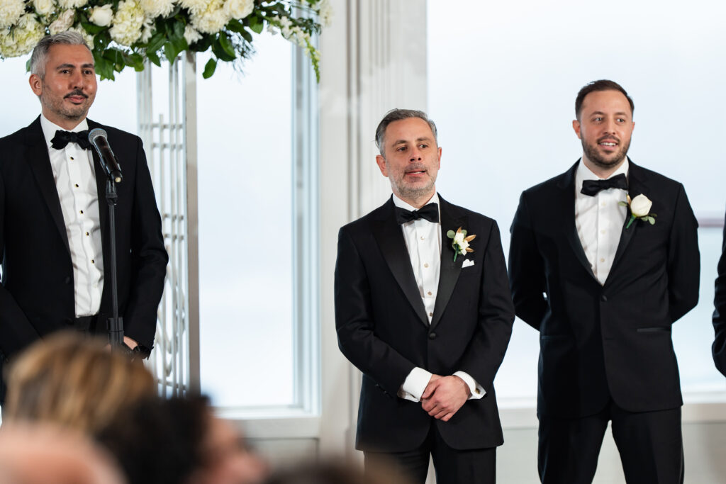 Four men in tuxedos captured by New Jersey Wedding Photographer Jarot Bocanegra standing in front of a microphone.