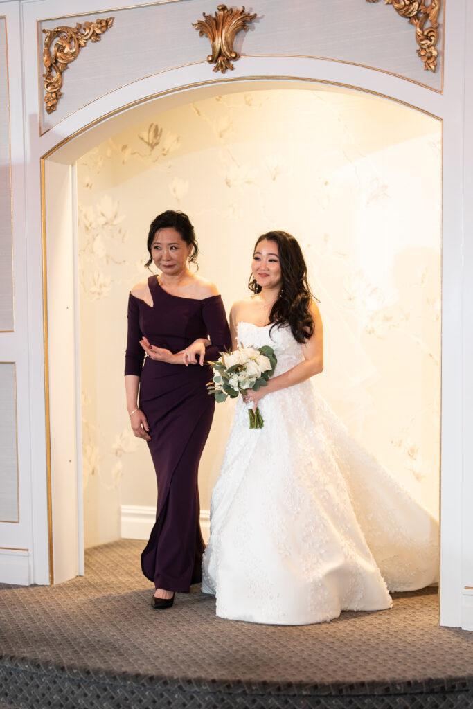 A bride and her mother, captured by New Jersey Wedding Photographer Jarot Bocanegra, walk through an archway.