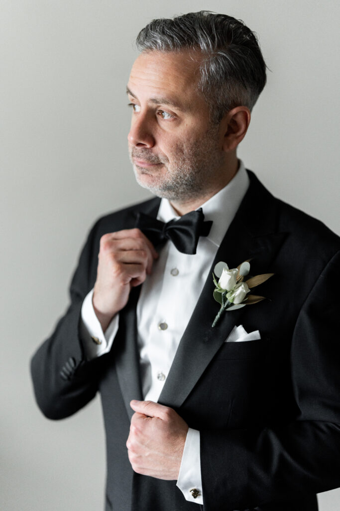 A man in a tuxedo adjusts his bow tie, captured by New Jersey Wedding Photographer Jarot Bocanegra.