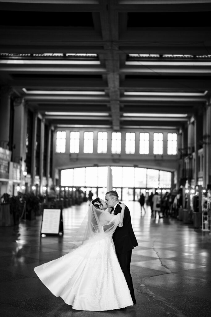 A bride and groom, captured by New Jersey Wedding Photographer Jarot Bocanegra, kissing in the middle of a large building.
