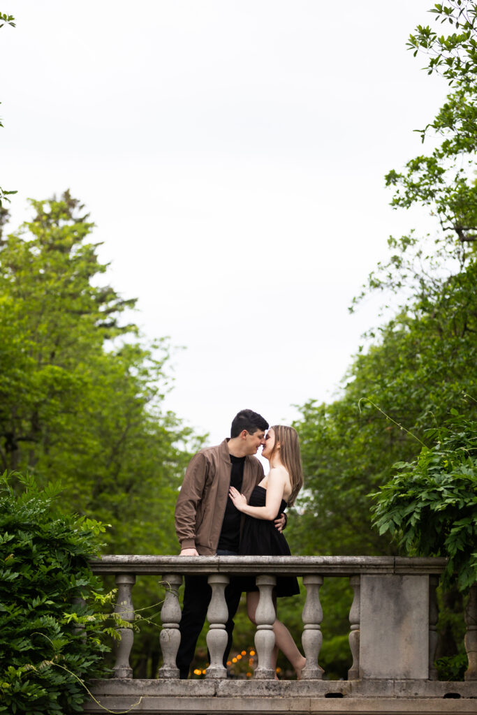 A couple captured by New Jersey Wedding Photographer Jarot Bocanegra, kissing on a railing at NJ Botanical Garden.