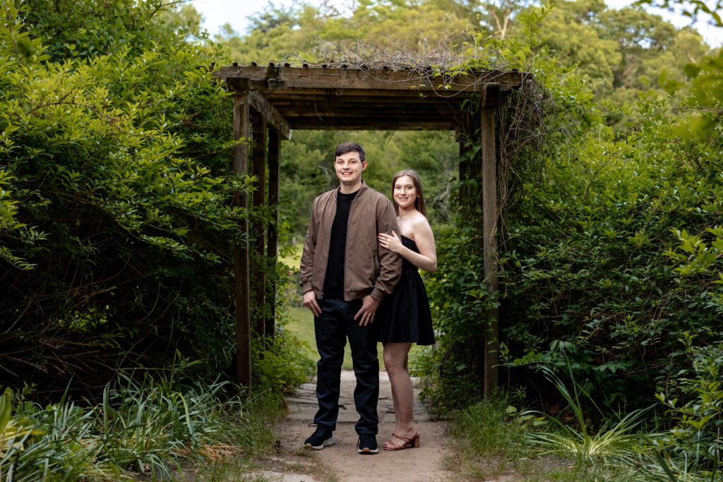A couple posing in front of an archway in a wooded area at New Jersey Botanical Garden during their engagement session, captured by New Jersey Wedding Photographer Jarot Bocanegra.