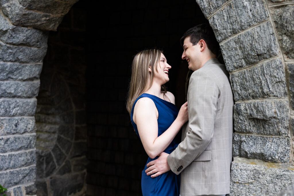 A couple smiling and embracing in a stone archway during their engagement session at New Jersey Botanical Garden, captured by New Jersey Wedding Photographer Jarot Bocanegra.