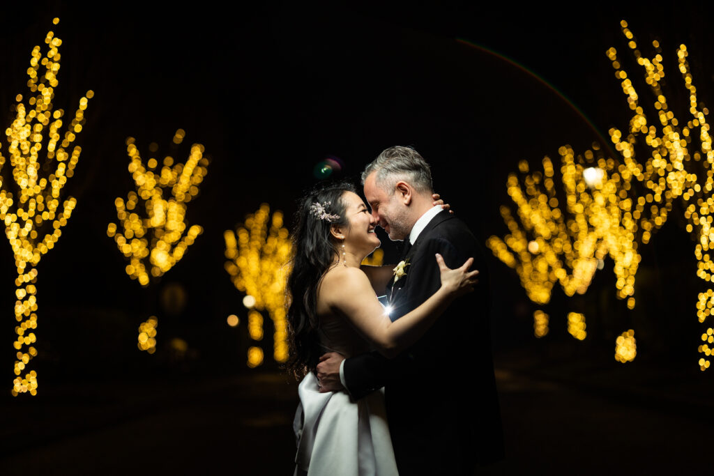 A bride and groom kiss in front of christmas lights at The Mill Lakeside Manor, captured by New Jersey Wedding Photographer Jarot Bocanegra.