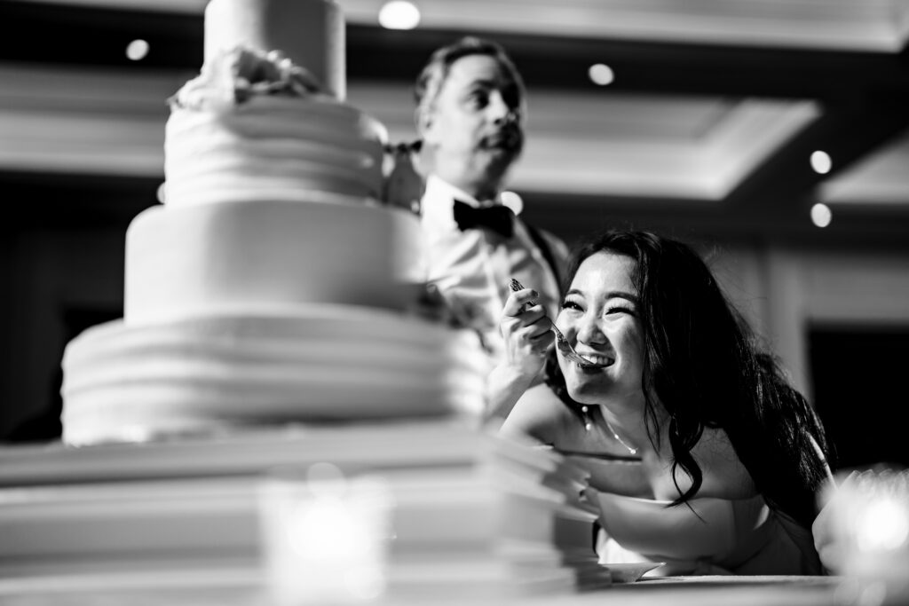 A bride and groom smiling cutting into the wedding cake during their wedding at The Mill Lakeside Manor, captured by New Jersey Wedding Photographer Jarot Bocanegra.