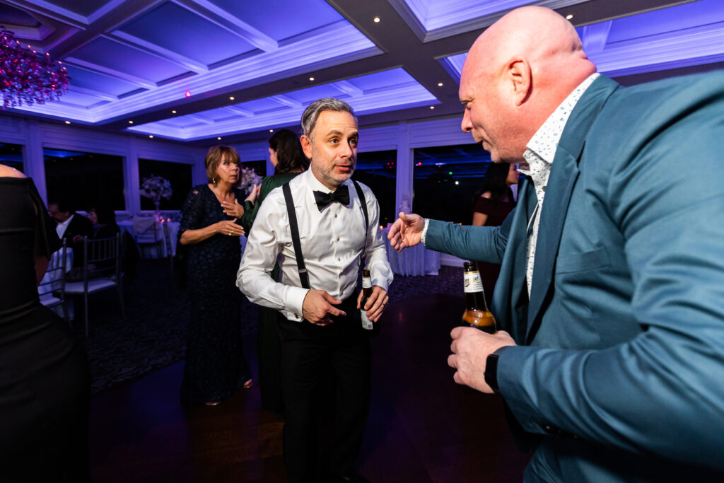 Groom in a tuxedo dancing and talking to another man at a wedding at The Mill Lakeside Manor, captured by New Jersey Wedding Photographer Jarot Bocanegra