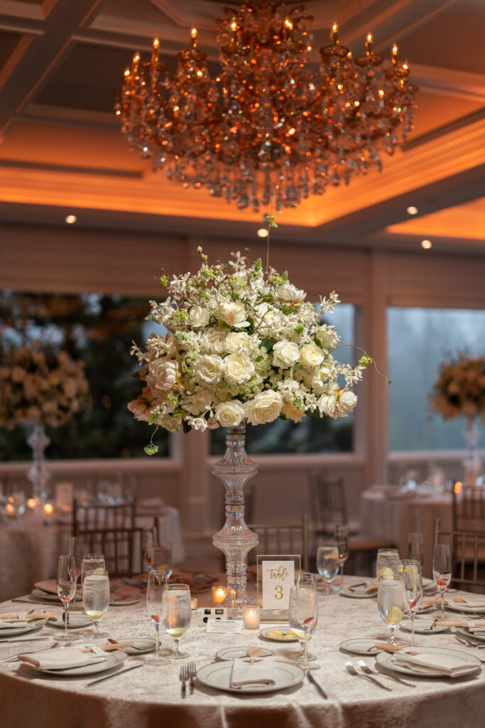 A table adorned with elegant white flowers, captured by New Jersey Wedding Photographer Jarot Bocanegra, is complemented by a dazzling chandelier.