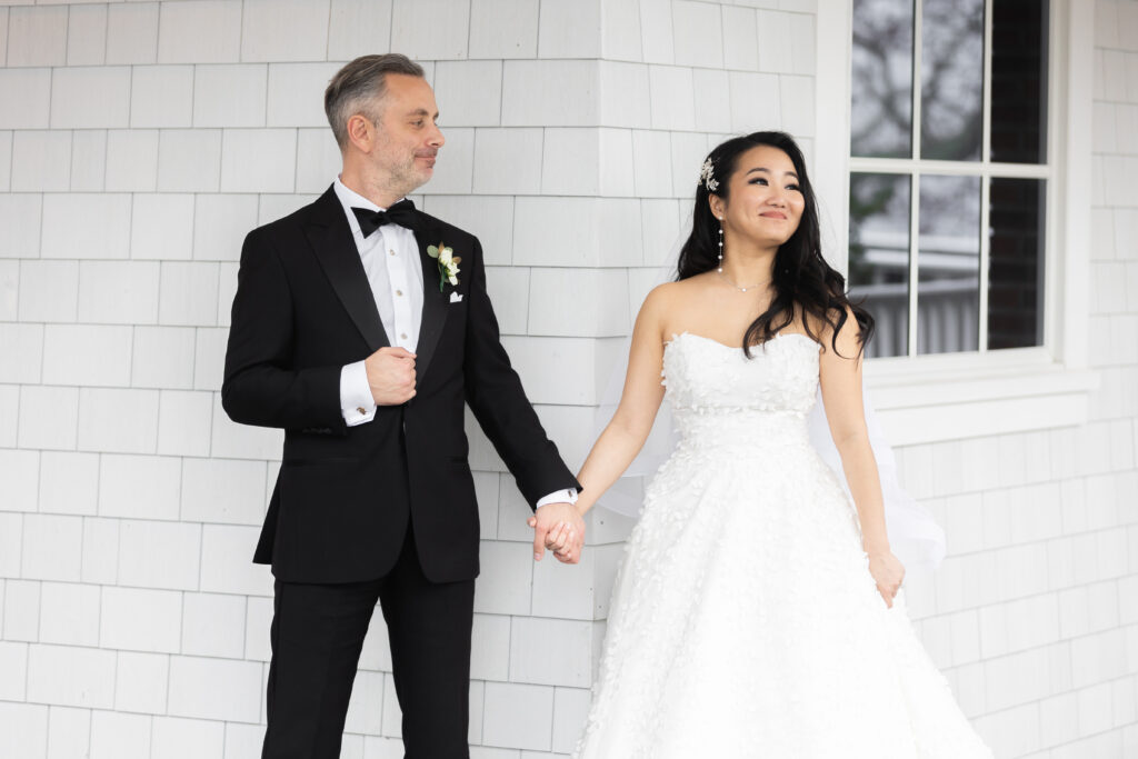 A bride and groom, captured by New Jersey Wedding Photographer Jarot Bocanegra, holding hands in front of a white house.